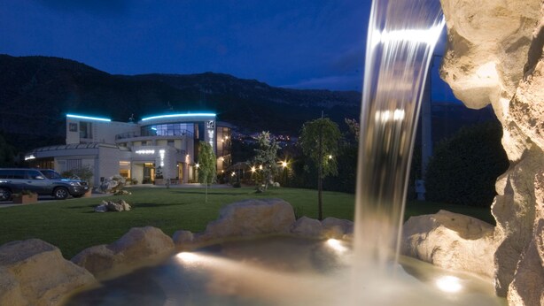 A waterfall feature in a landscaped area with a building in the background. - Hotel Le Ginestre (Roccacasale)