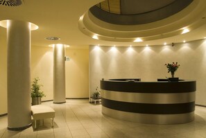 A reception area with a circular desk, two columns, a bench, and potted plants. - Hotel Le Ginestre (Roccacasale)