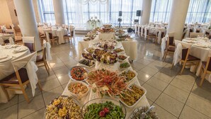 A banquet hall with multiple round tables set for a formal event, featuring a variety of dishes and a central display of seafood. - Hotel Le Ginestre (Roccacasale)