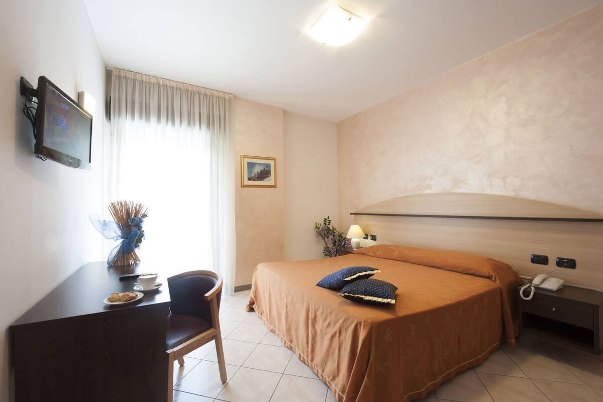 Habitación de hotel con cama, escritorio, silla, televisor y teléfono en la mesita de noche.