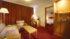 Habitación de hotel con alfombra roja, sofá, mesa, escritorio con silla y armario.
