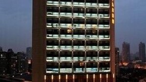 Un hotel moderno de gran altura con varios pisos, amplias ventanas y una entrada destacada en la parte superior.