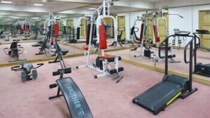 Un gimnasio con diversas máquinas de ejercicio, espejos y una cinta de correr.