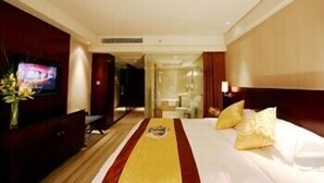 Habitación de hotel con una cama grande, un televisor a la izquierda y un baño visible a través de una puerta abierta.