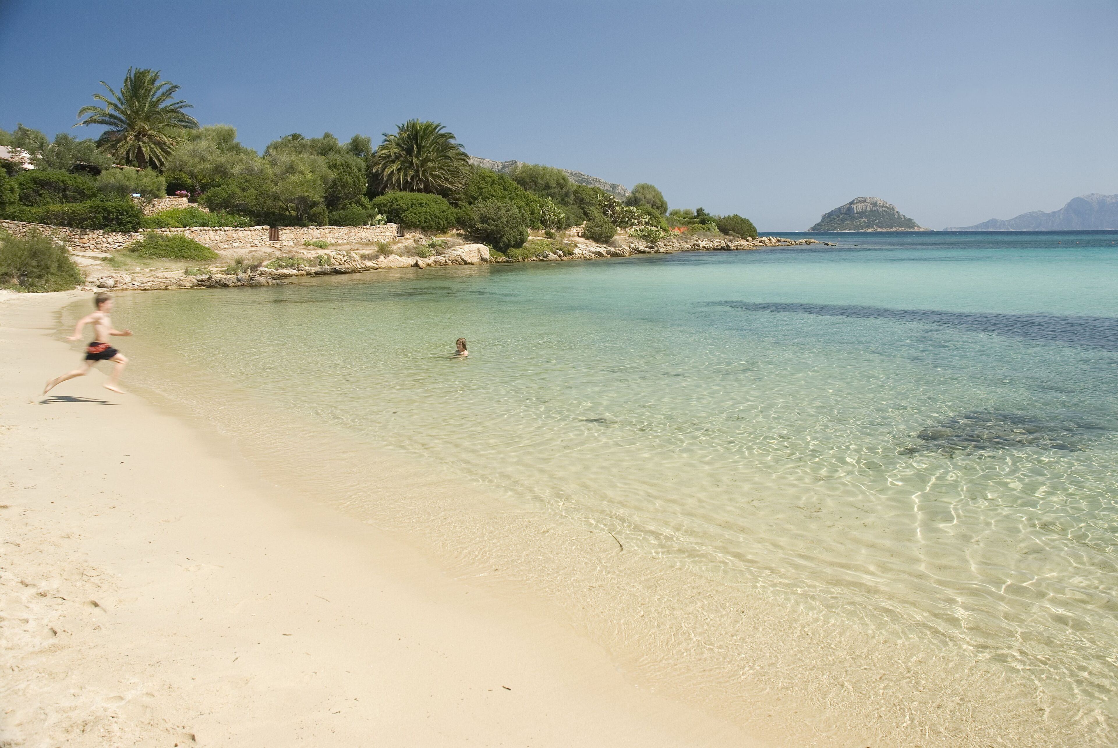 Ein Strand mit klarem Wasser, sandigem Ufer und einer Person, die rennt.