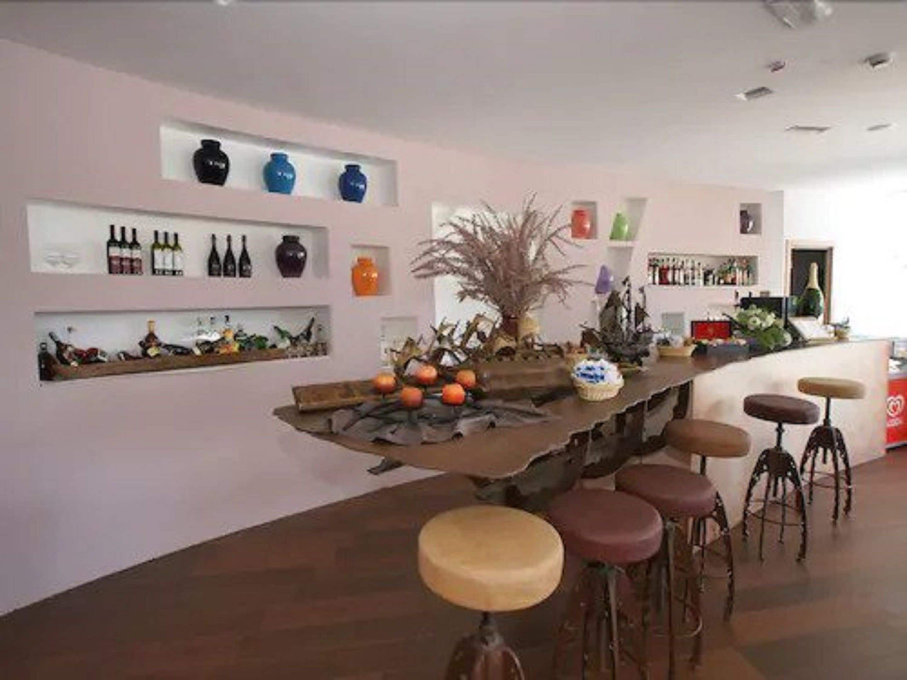A modern bar area with a long counter, stools, and shelves displaying bottles and decorative items.