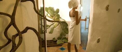 A person in a white towel standing at a door, with a cactus plant and a decorative metal structure in the background.
