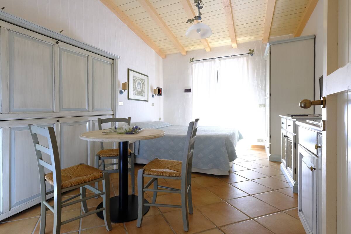 A room with a bed, a table with chairs, and a kitchenette.