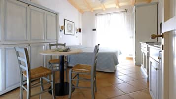 A room with a bed, a table with chairs, and a kitchenette.