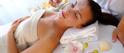 A person lying on a bed with a towel, a face mask, and a seashell.