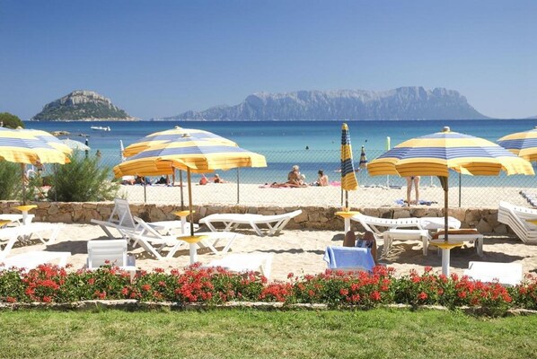 A beach with sun loungers and umbrellas, a stone wall, and a clear view of the sea and distant mountains. - Residence Baia Caddinas (Golfo Aranci)