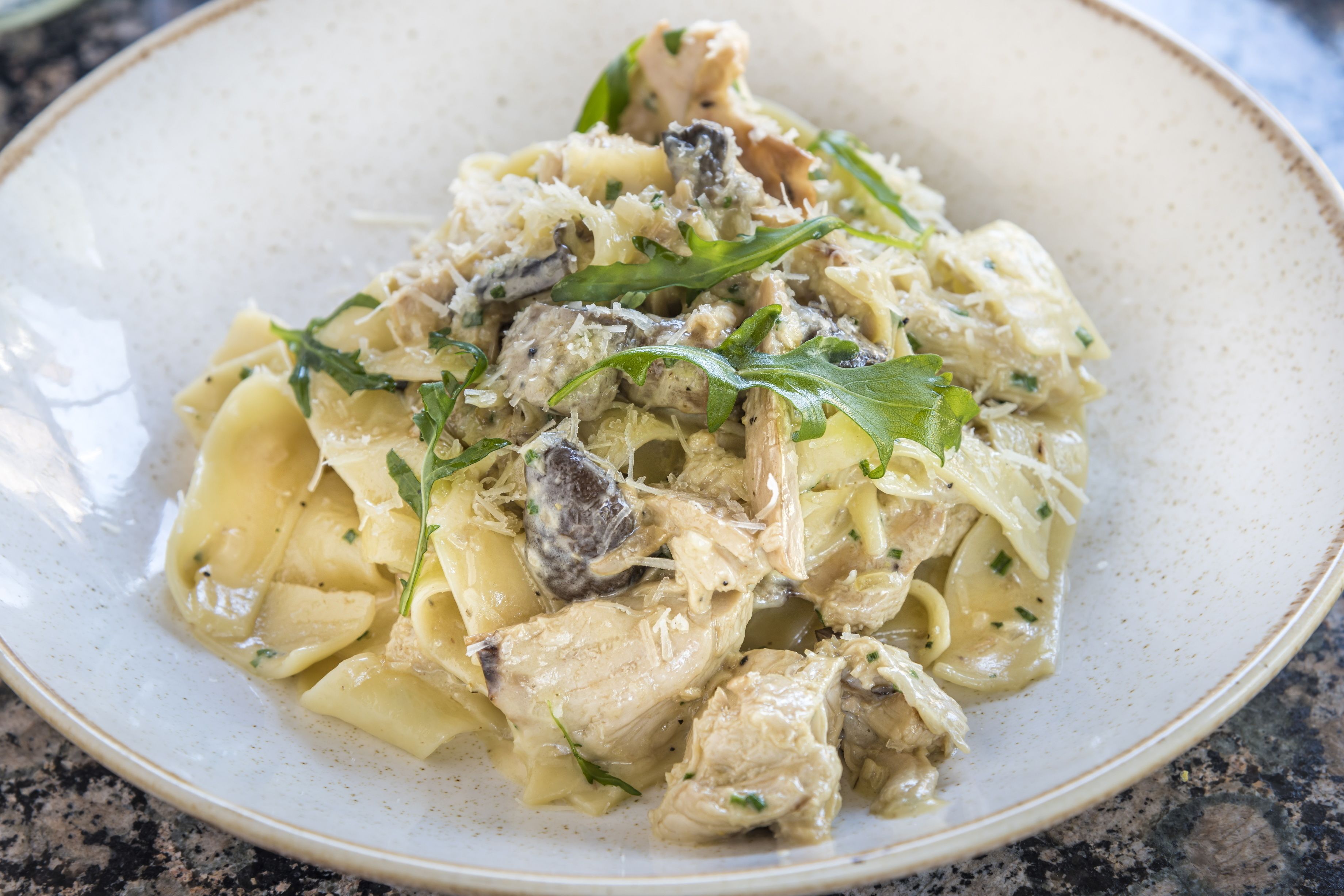 A plate of pasta with chicken and mushrooms, garnished with herbs.
