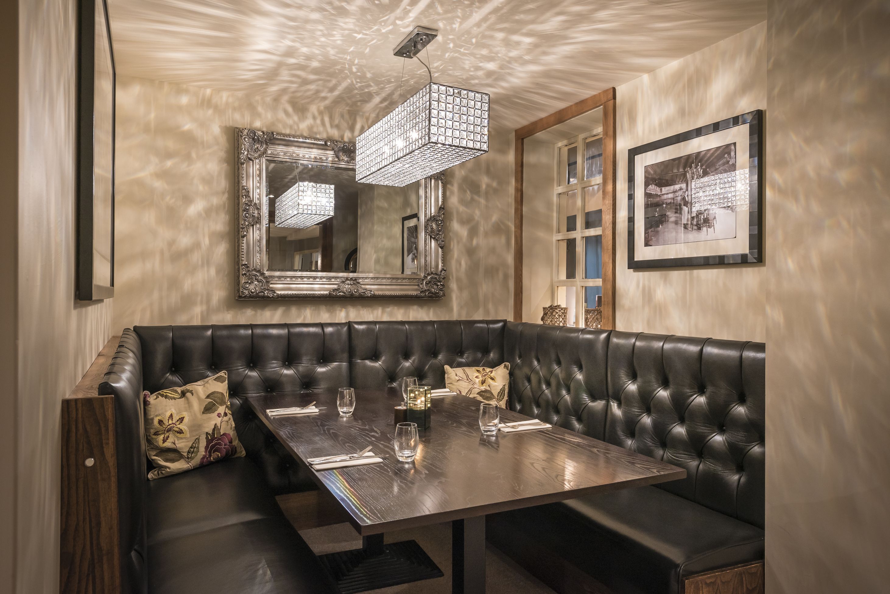 A dining area with a wooden table, black leather booth seating, and a large mirror above.