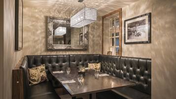 A dining area with a wooden table, black leather booth seating, and a large mirror above.