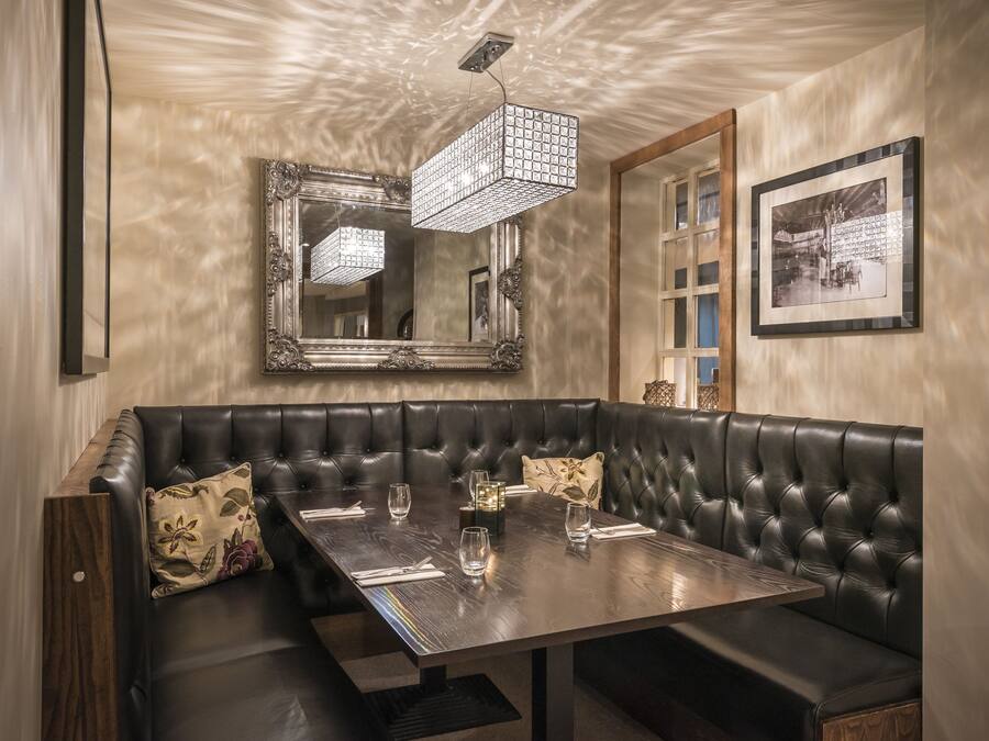 A dining area with a wooden table, black leather booth seating, and a large mirror above.