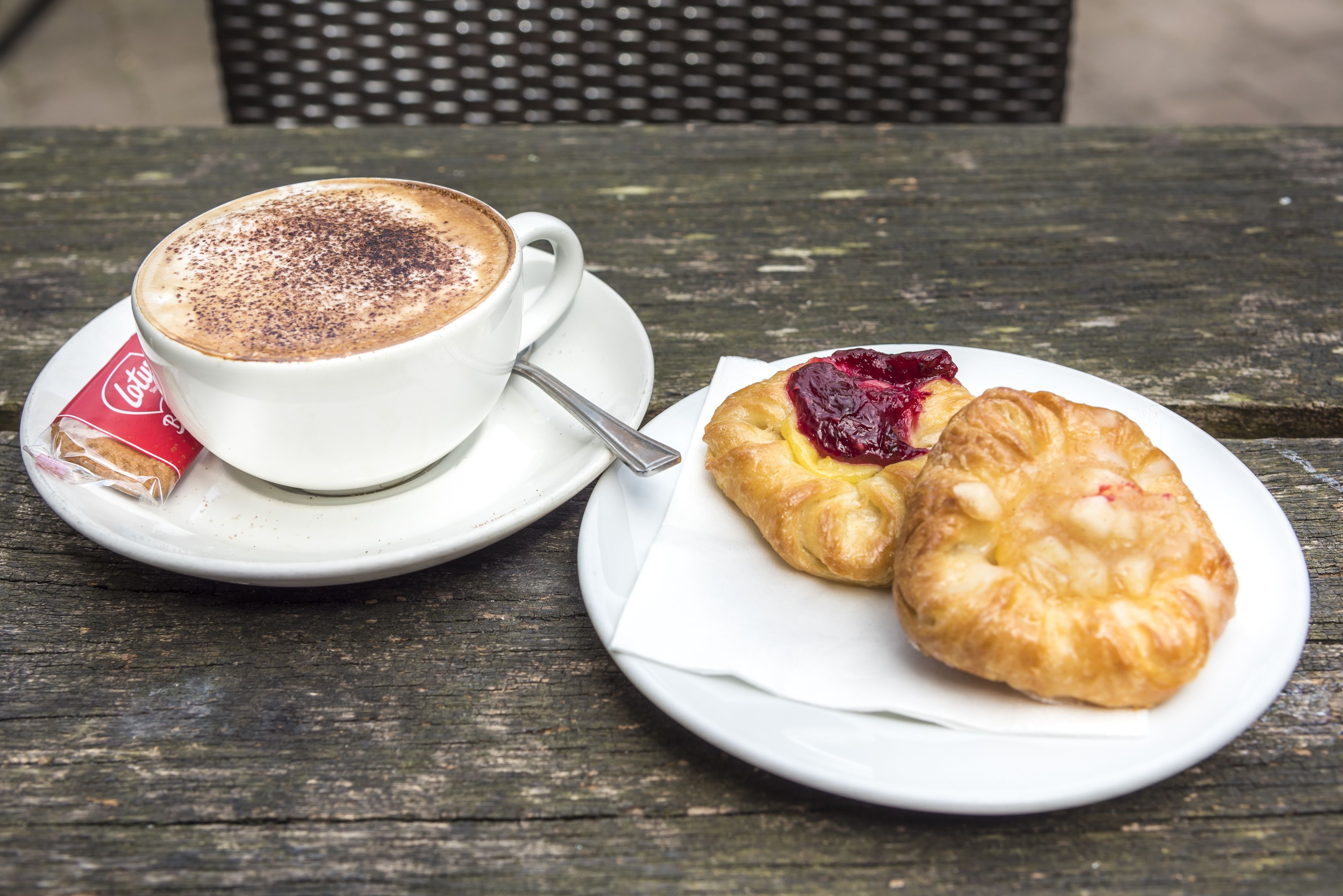 A cup of coffee with a chocolate topping and a pastry with jam on a wooden table.