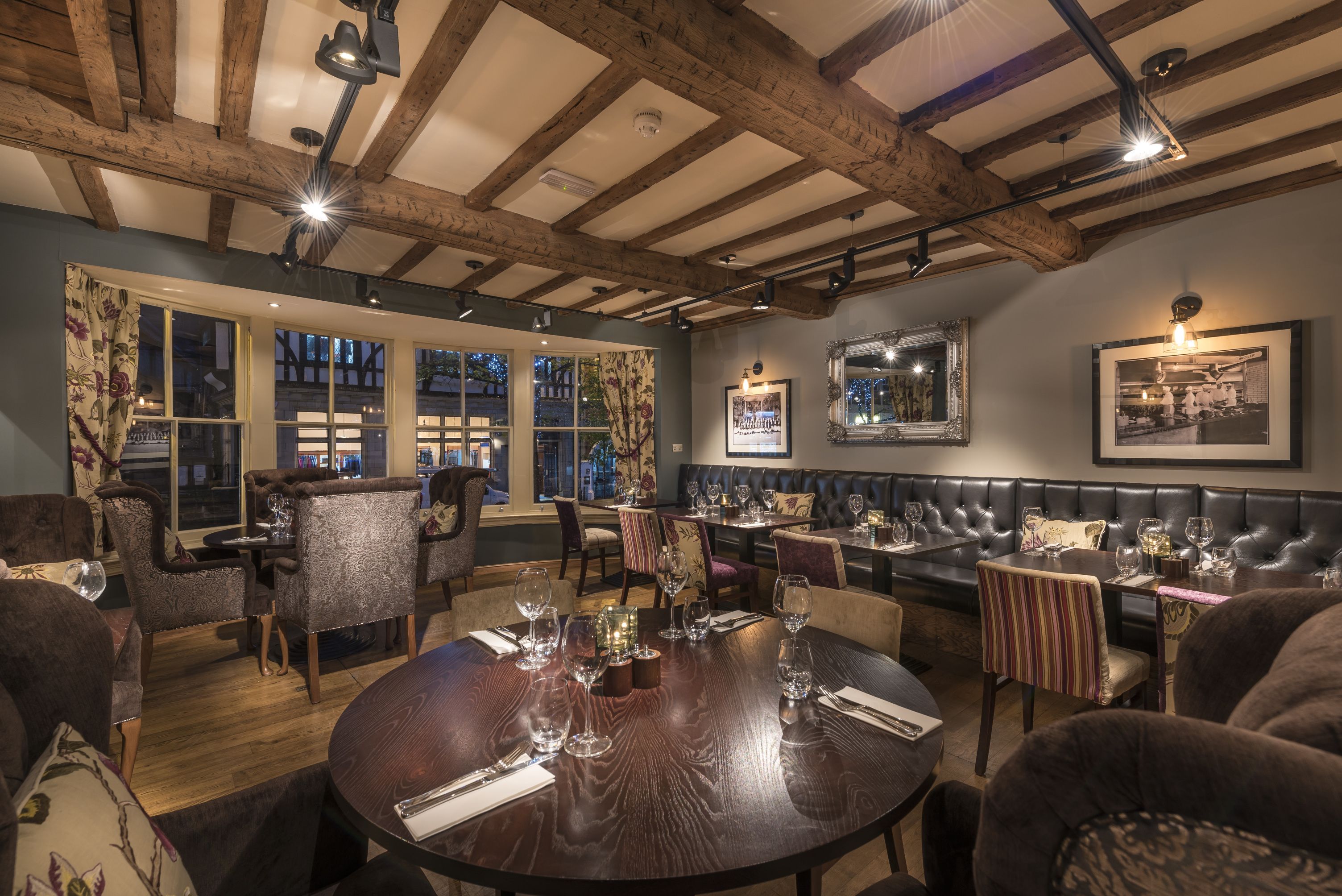 A restaurant with wooden beams, round tables, and cushioned seating.