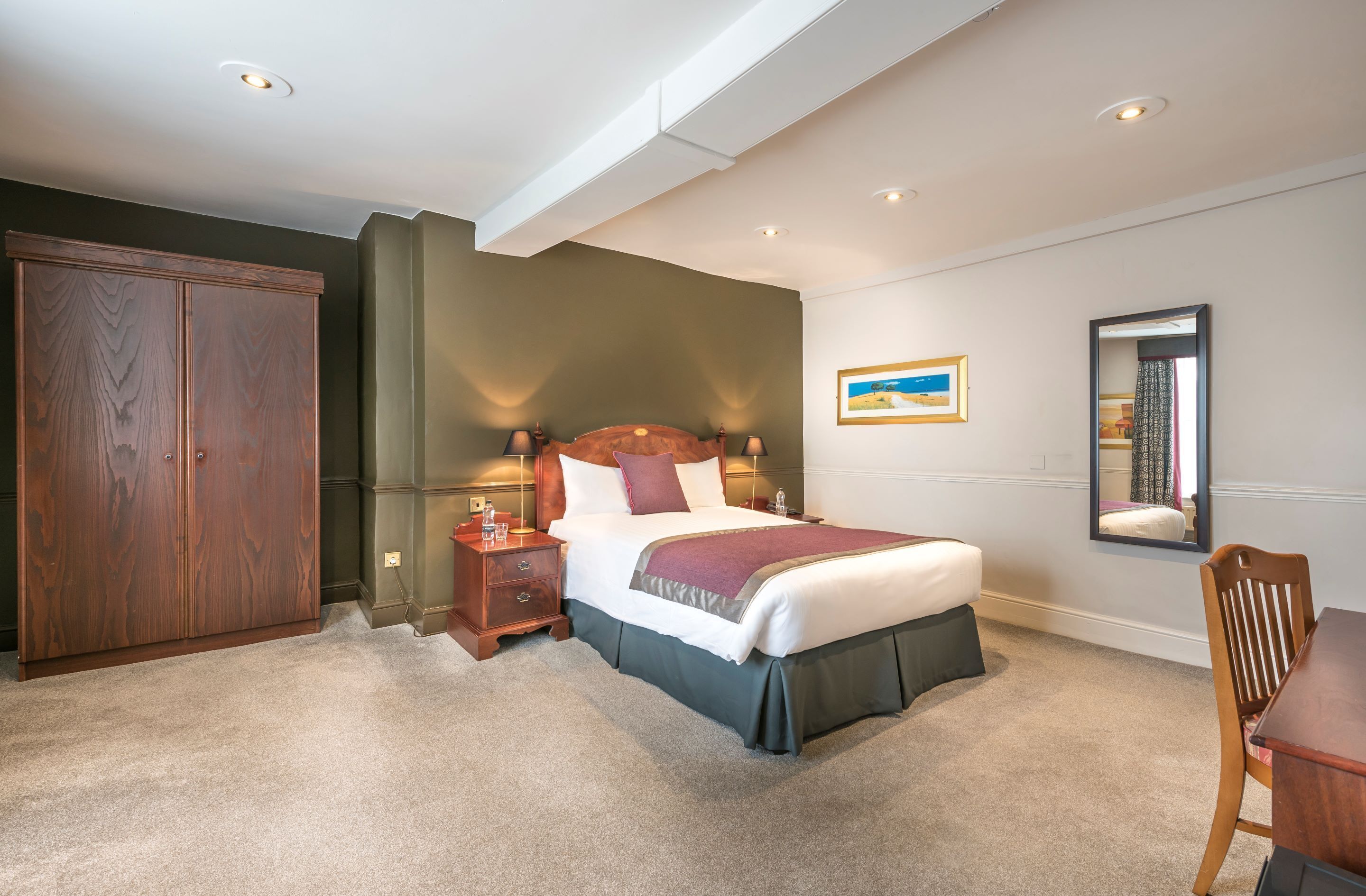 A bedroom with a large bed, a wooden wardrobe, a nightstand, and a mirror on the wall.