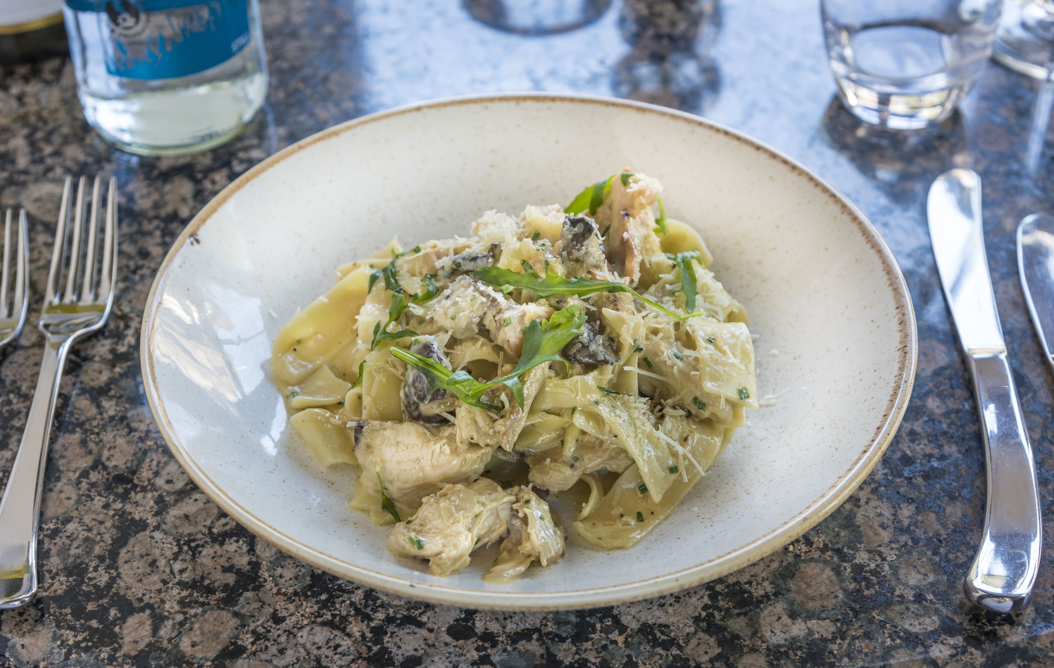 Ein Teller Pasta mit Hähnchen und Gemüse auf einer gefleckten Arbeitsplatte.
