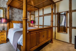 Una cama con dosel y tablero de madera, una mesita de noche con lámpara y un espejo en la pared.