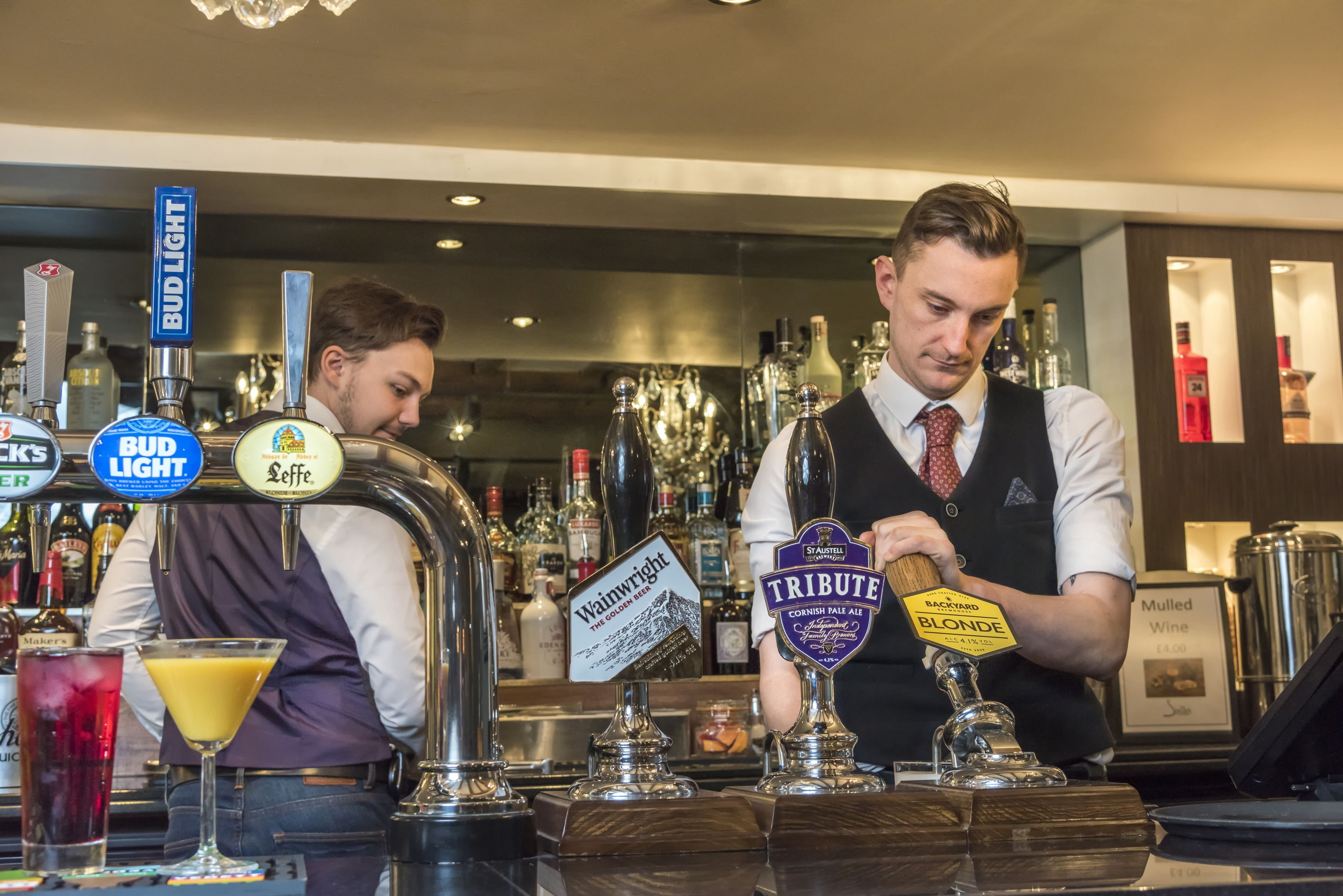 Zona de bar con grifos de cerveza identificados como 'Bud Light', 'Leffe', 'Wainwright' y 'Tribute'.