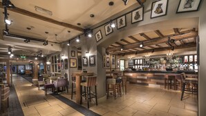 A bar area with wooden beams, bar stools, and a well-lit space with framed pictures on the walls.