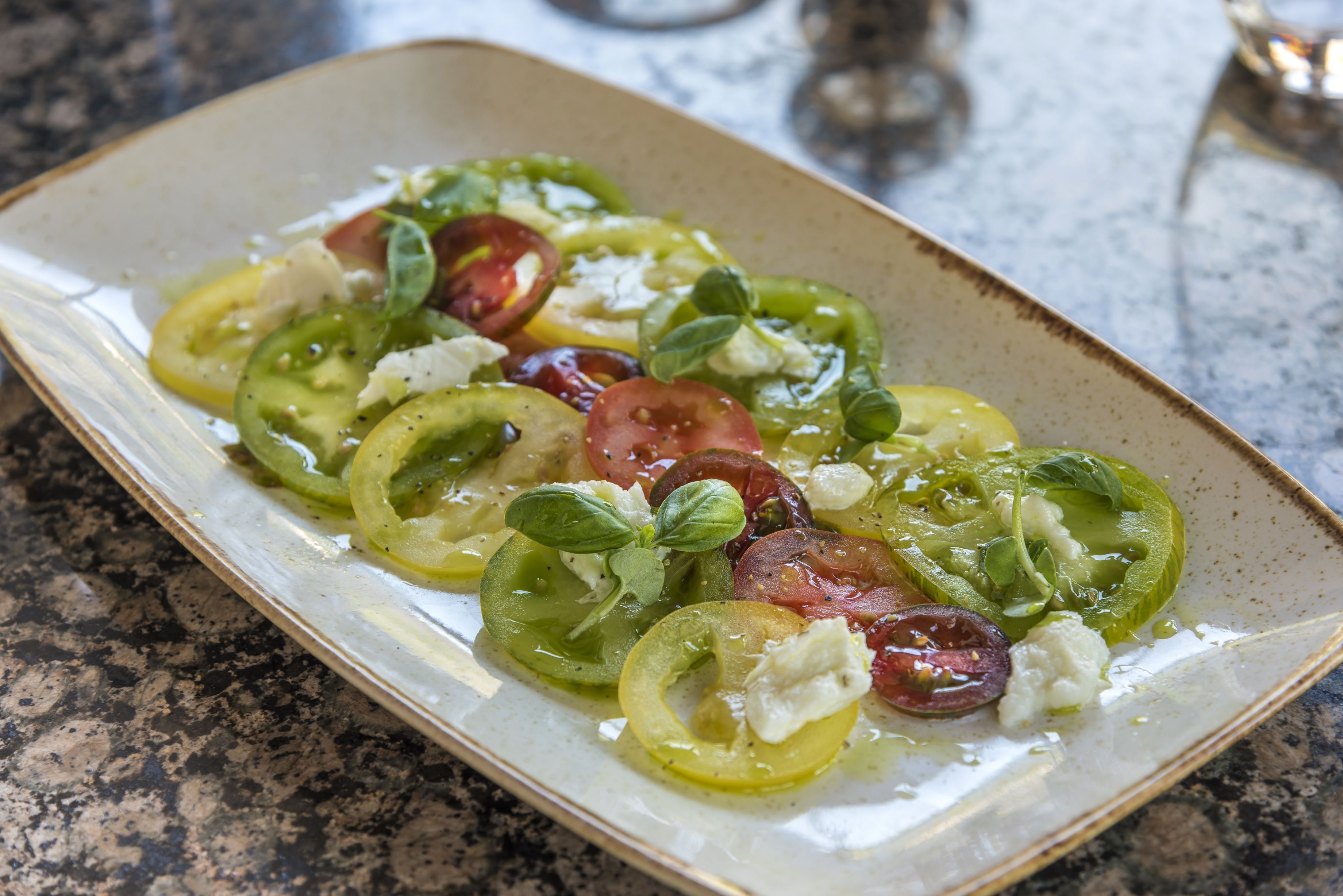 A rectangular ceramic plate with a salad consisting of sliced tomatoes, green peppers, and cheese, garnished with basil leaves.