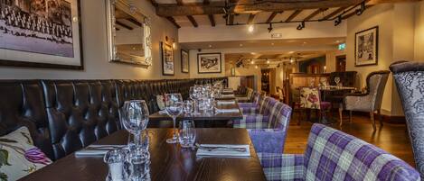A restaurant with wooden beams, leather booths, and plaid-patterned seating. Tables are set with glasses and cutlery.