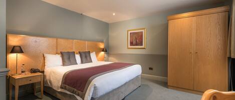 A bedroom with a bed, bedside table, lamp, wardrobe, and a framed picture on the wall.