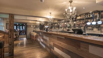 A bar area with wooden flooring, a bar counter, and a chandelier.