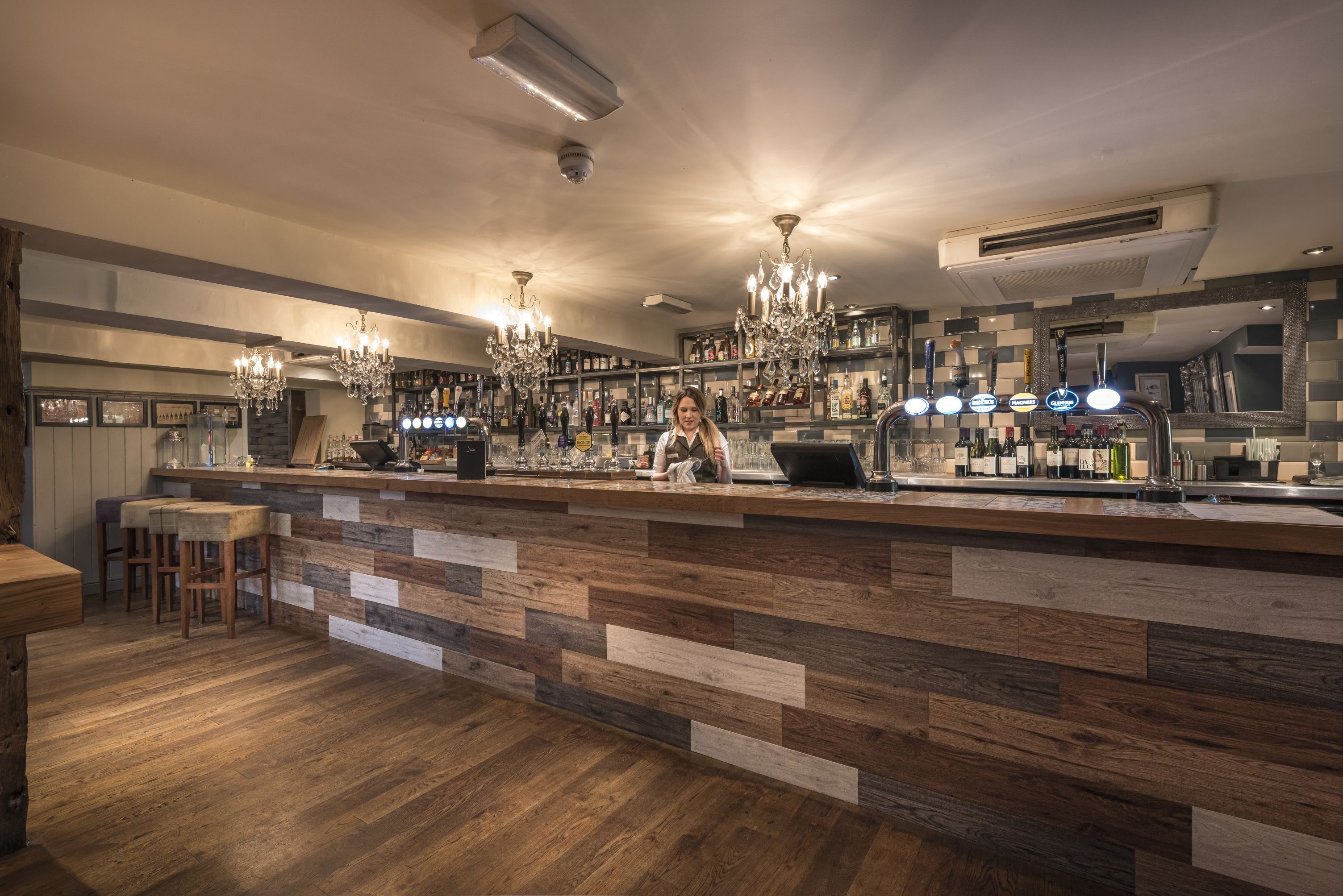 Un bar avec un comptoir en bois, des tabourets et des lustres.