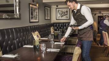 Ein Restaurant mit einem langen Holztisch, schwarzen Ledersitzbänken und gerahmten Bildern an den Wänden.