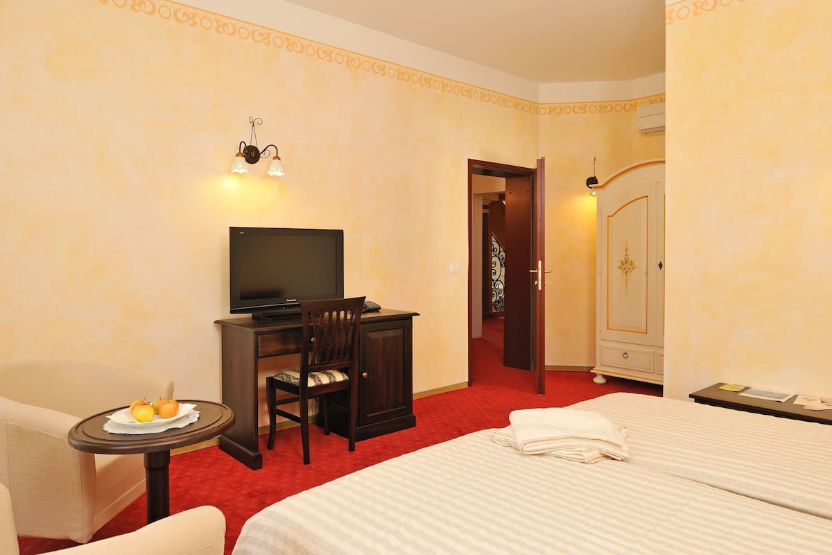 A hotel room with a bed, a desk with a television, a chair, a small table with apples, and a wardrobe.