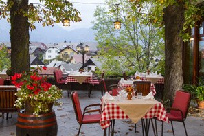 An outdoor dining area with tables set for two, surrounded by trees and a view of buildings in the background. - Gostilna Lectar (Radovljica)