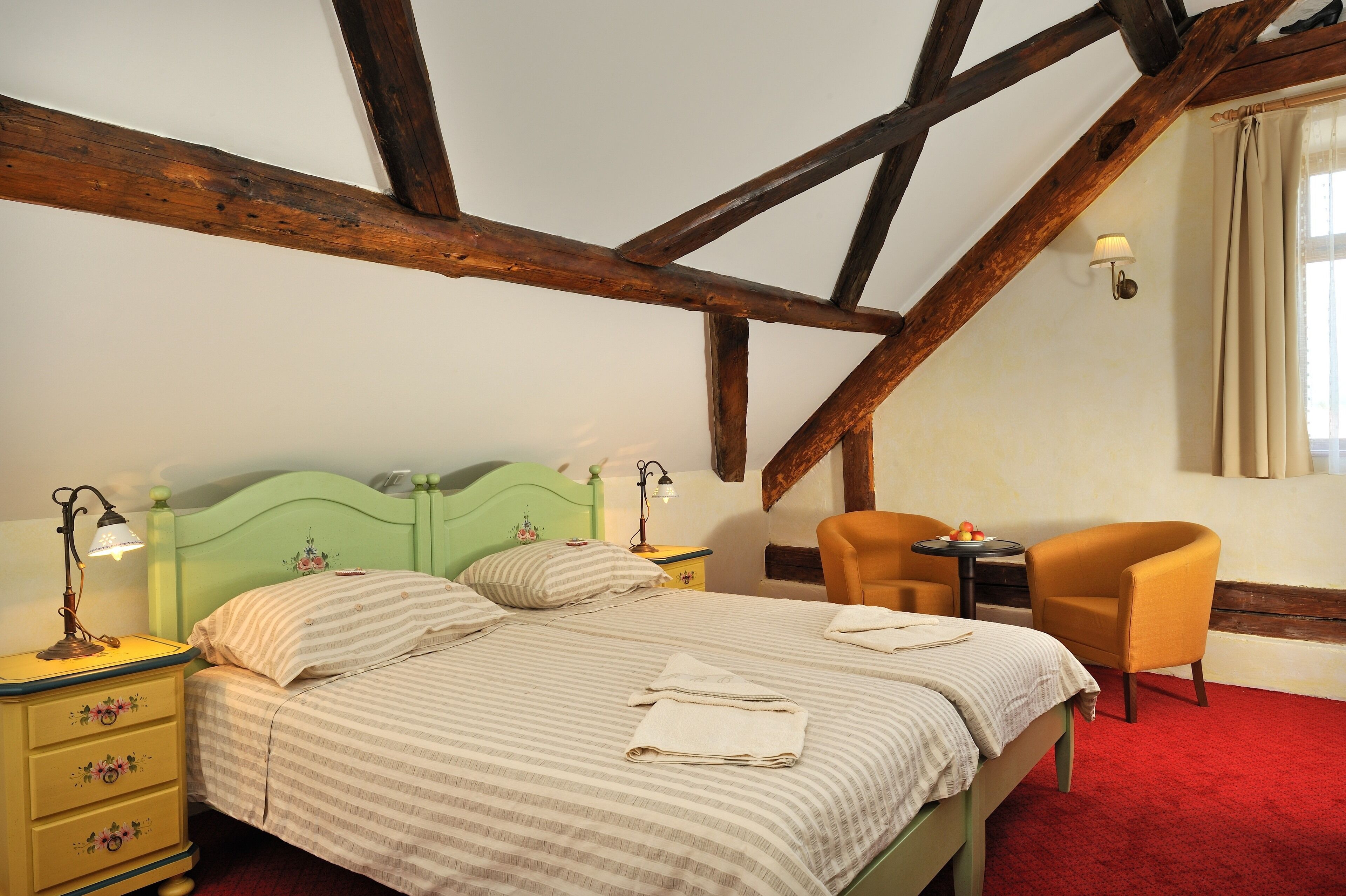 Een kamer met een bed, twee nachtkastjes met lampen, een stoel en een kleine tafel met een lamp.
