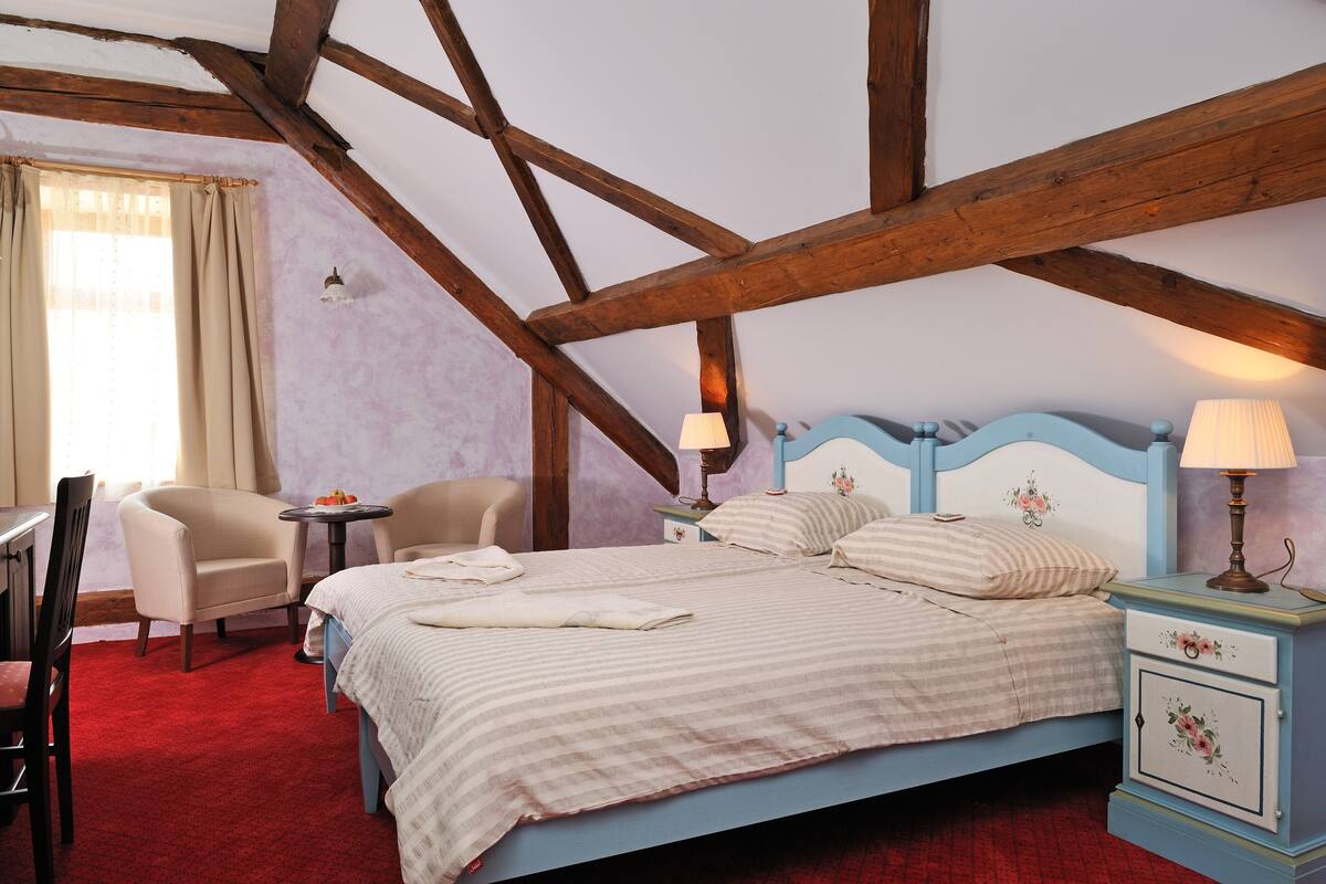 A bedroom with a bed, two chairs, a small table, and a nightstand with lamps.