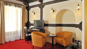 A hotel room with a red carpet, two orange armchairs, a small table with a lamp, a television, and a sewing machine. - Gostilna Lectar (Radovljica)