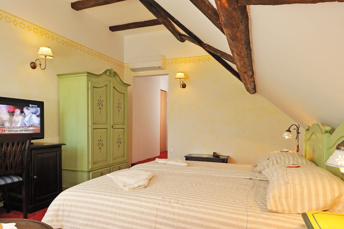 A bedroom with a bed, a television, a wardrobe, and two wall-mounted lamps.