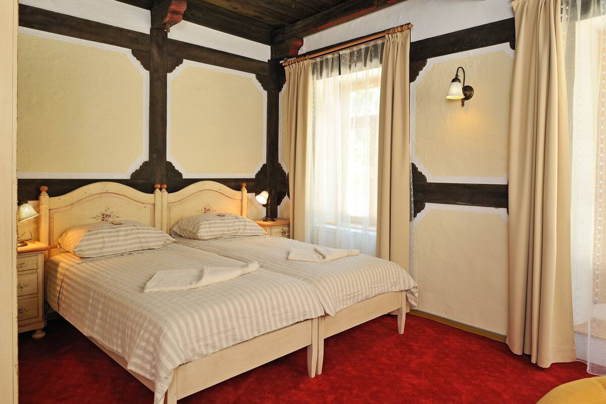 A bedroom with a double bed, wooden headboard, a nightstand with a lamp, and a red carpet.