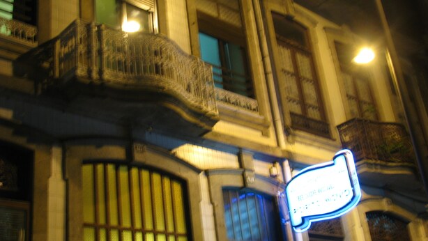 Een gevel met een groot, versierd balkon en een neonreclame.
