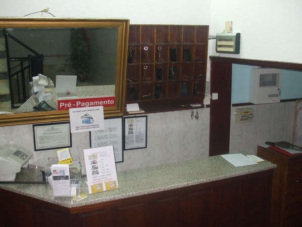 Zona de recepción de hotel con mostrador de madera, un espejo, un cartel que indica las opciones de pago y un perchero para llaves.
