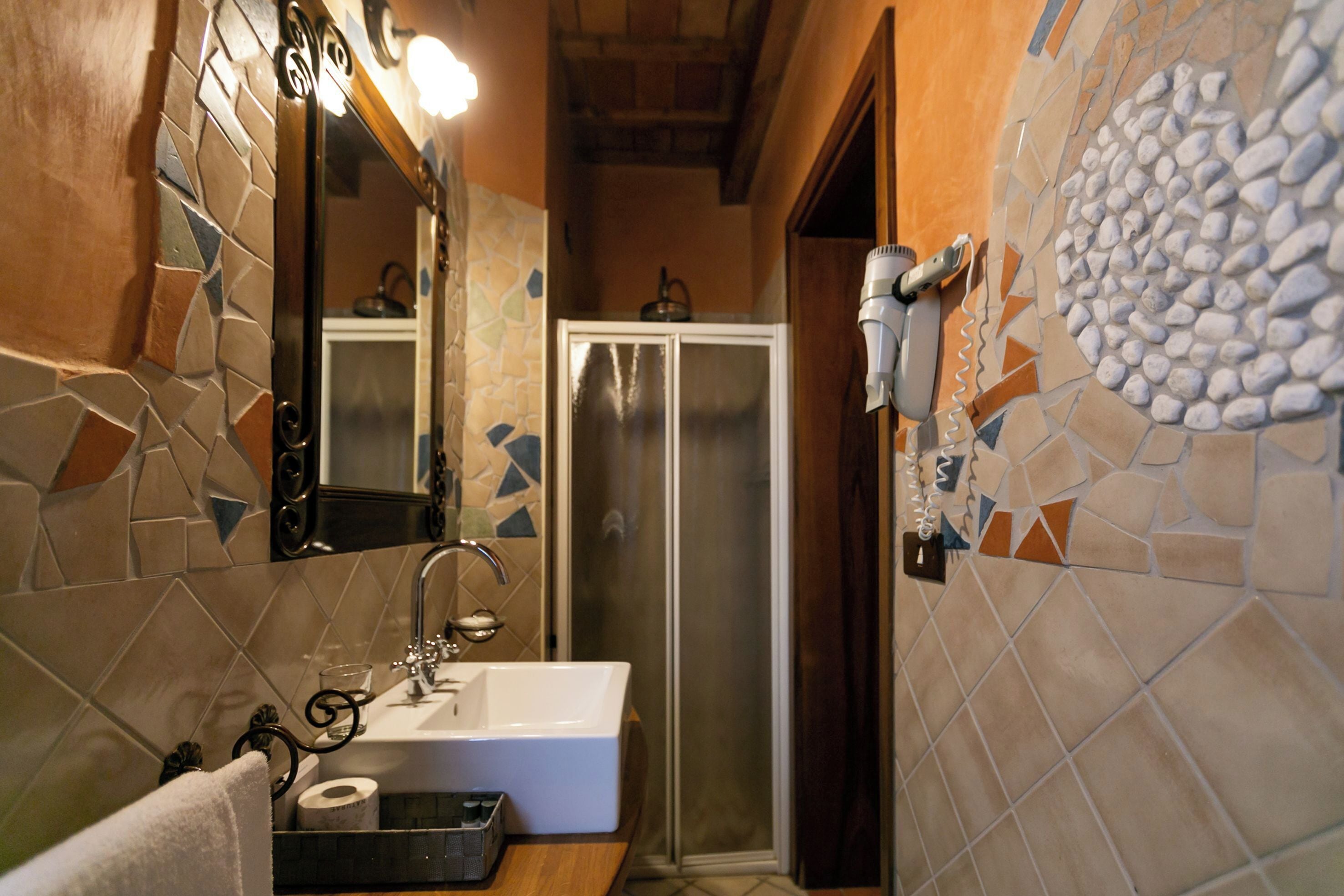Un baño con pared de azulejos, un lavamanos, un espejo, una toalla y una puerta de ducha.