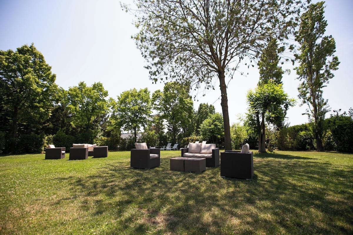 An outdoor seating area with multiple sofas and chairs arranged on a grassy lawn, surrounded by trees.