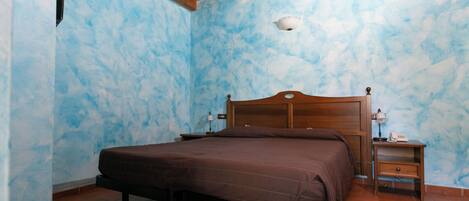 A bedroom with a wooden bed, a nightstand with a lamp, and a blue textured wall.