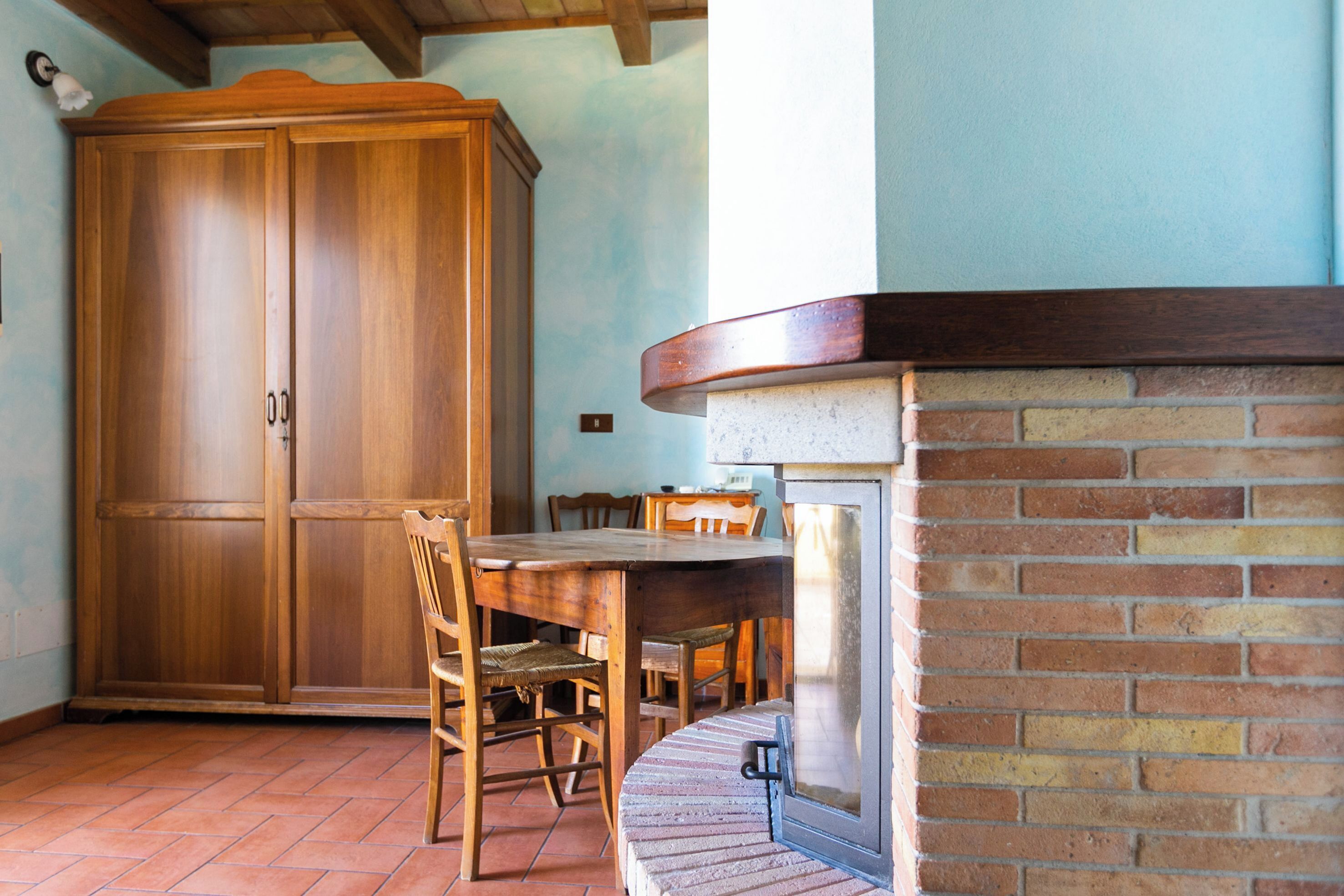 A dining area with a wooden table and chairs, a brick fireplace, and a large wooden cabinet.