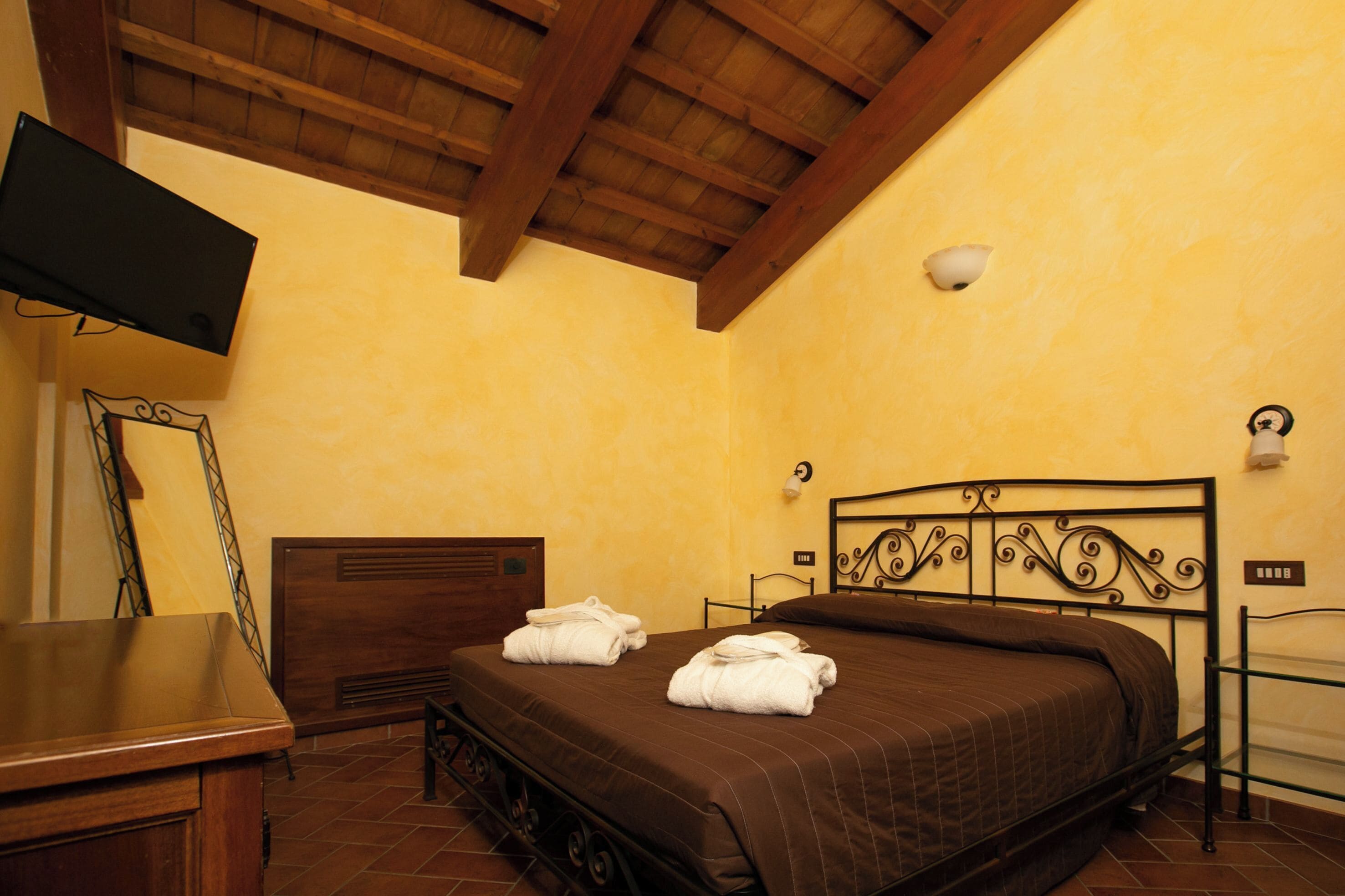 A hotel room with a bed, a desk, a television, and a wall-mounted light fixture.