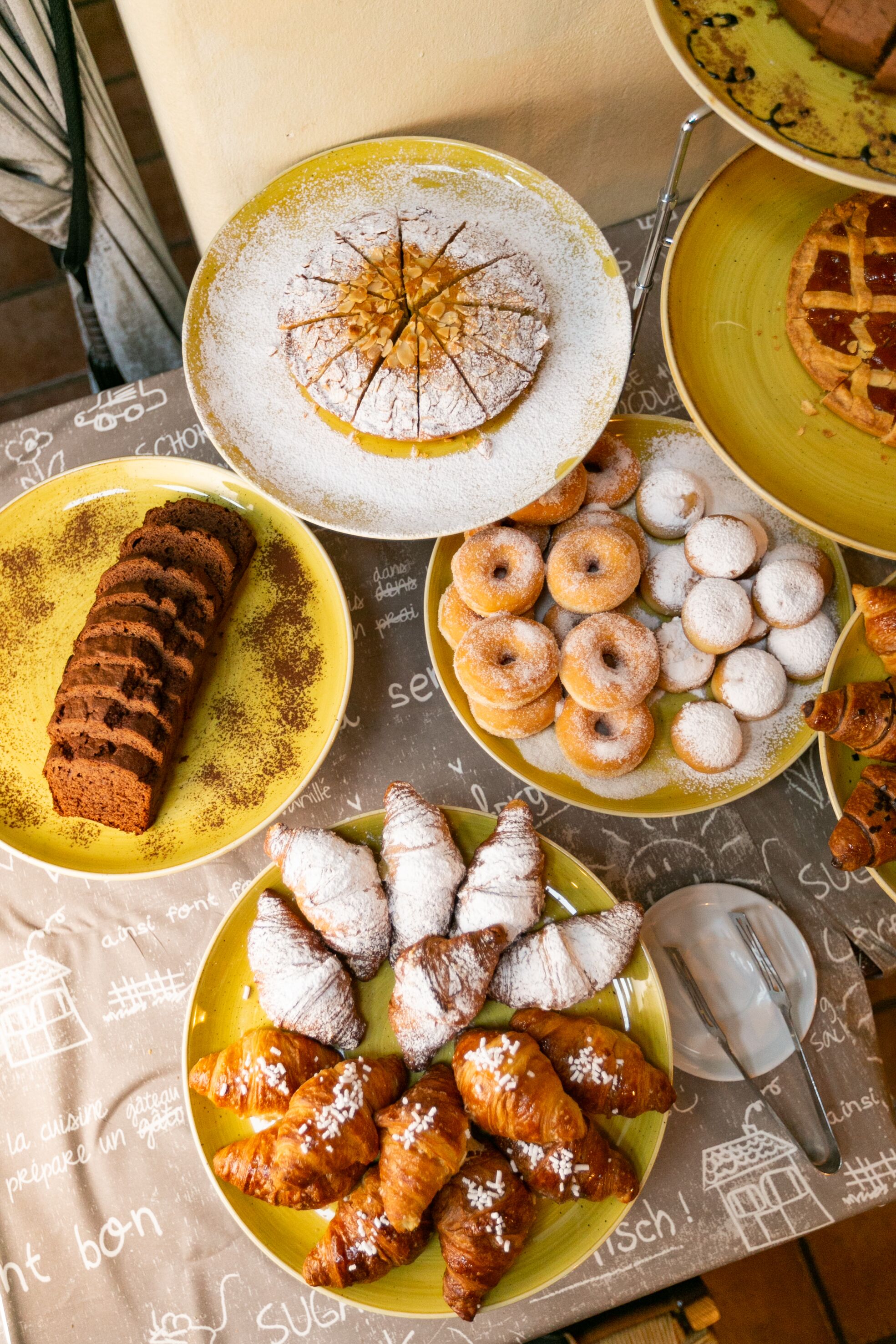 A table with various pastries and desserts, including a cake, donuts, and croissants.