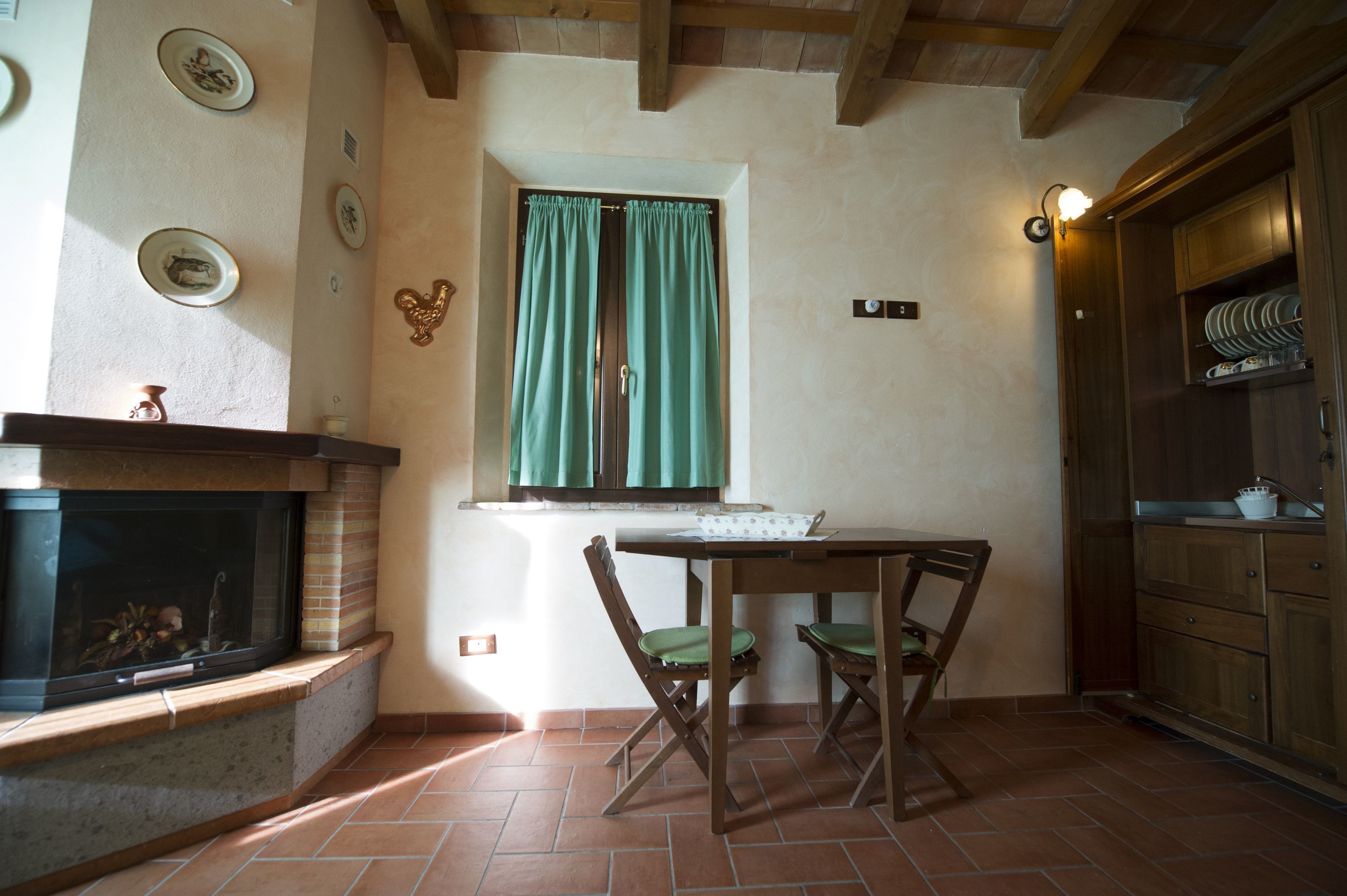 A room with a fireplace, a dining table with chairs, a window with curtains, and wooden cabinets.