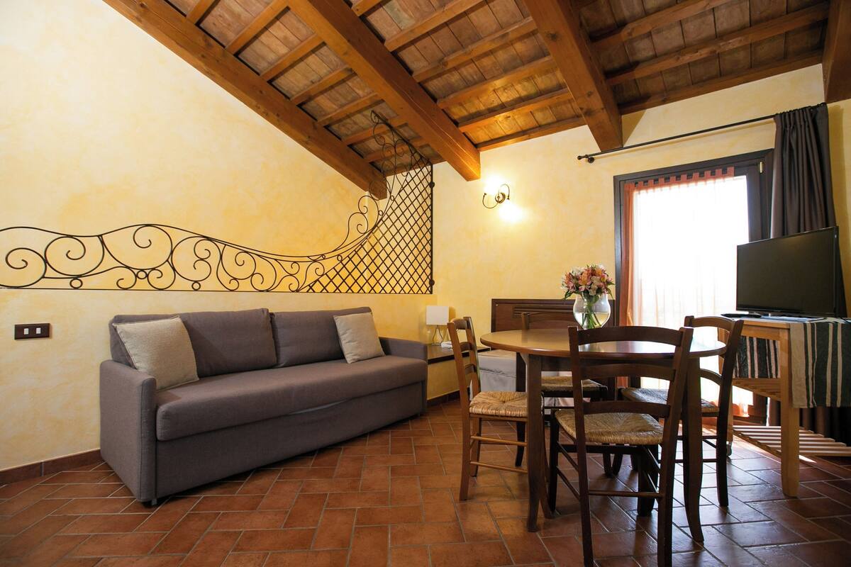 A cozy living room with a sofa, wooden dining table, chairs, and a TV.