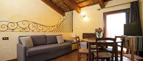 A cozy living room with a sofa, wooden dining table, chairs, and a TV.